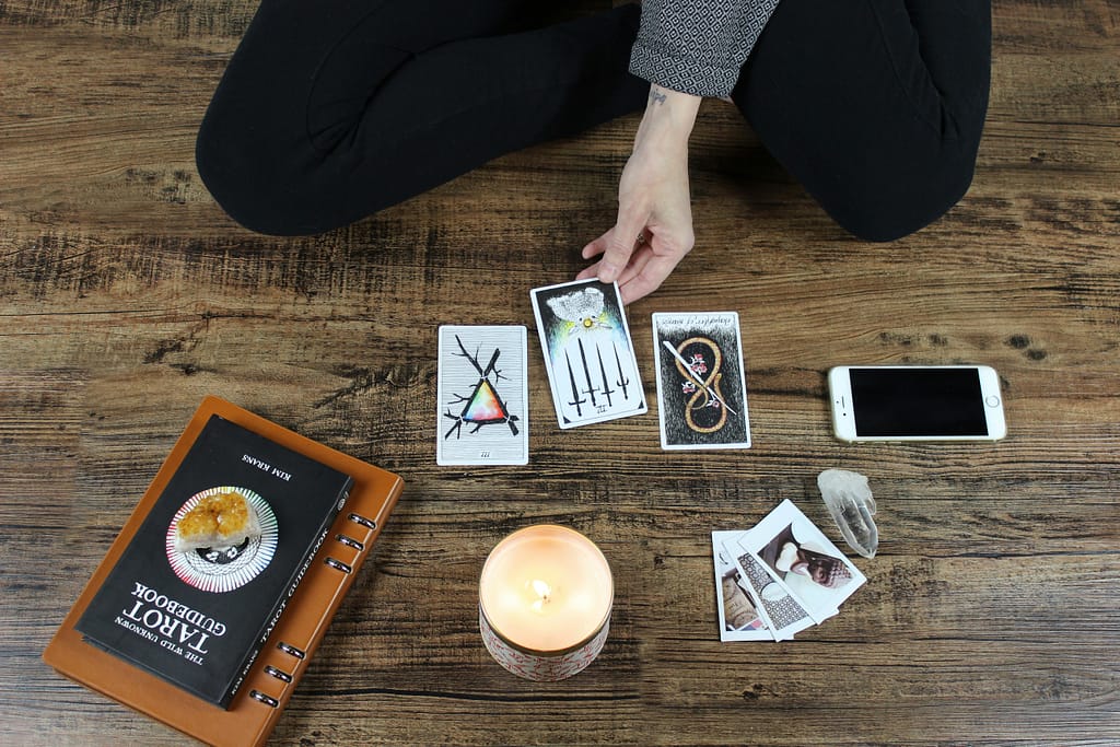 a person performing a tarot reading with three cards laid out on the floor, surrounded by a guidebook, a candle, and crystals