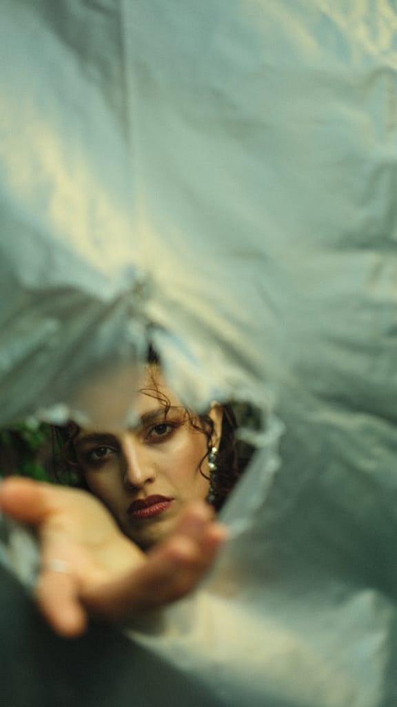 Symbolic image of a person reaching through a torn veil, representing the High Priestess tarot card&rsquo;s themes of divine mystery and the veil of the temple.

