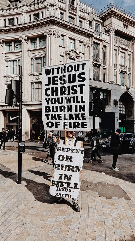 Street preacher in a busy city centre holding large signs that read &ldquo;Without Jesus Christ you will burn in the lake of fire&rdquo; and &ldquo;Repent or burn in hell.&rdquo;