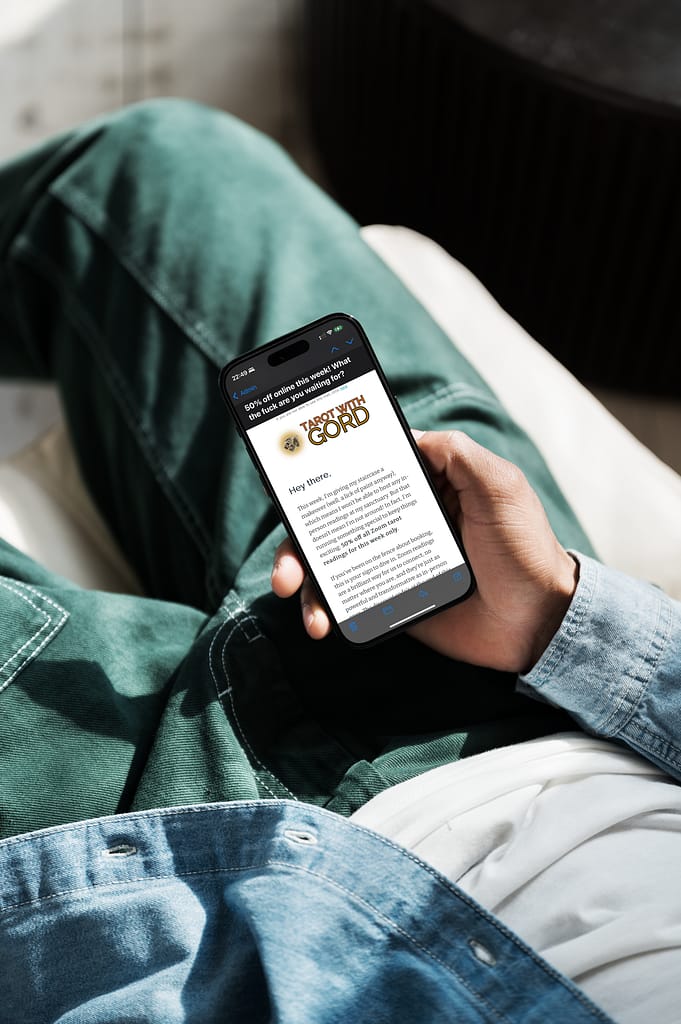 A person lounging on a couch, holding a smartphone displaying an email from Tarot With Gord, showcasing exclusive offers and updates.