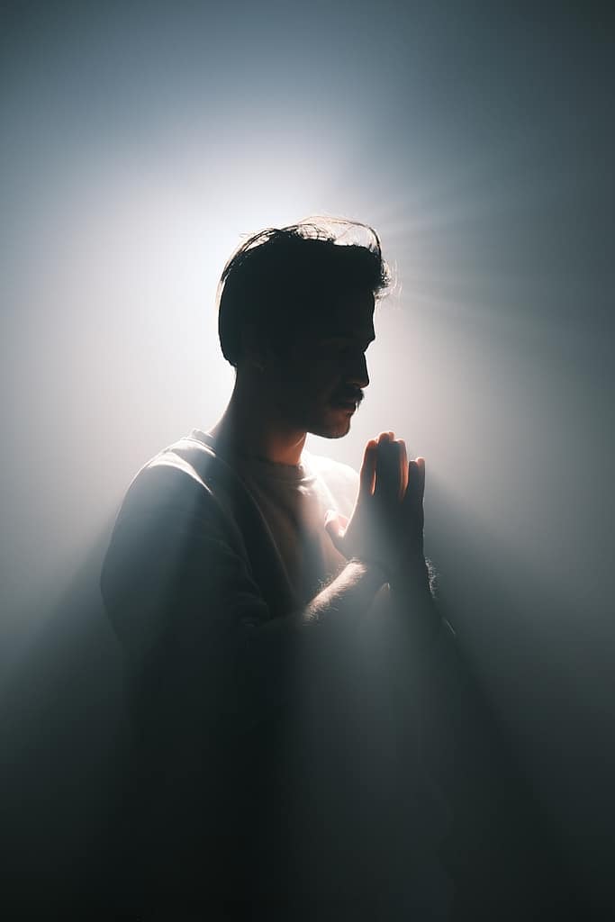 Man standing in soft light with hands pressed in reflection, symbolising how tarot helps people navigate spiritual shifts and real-life turning points.