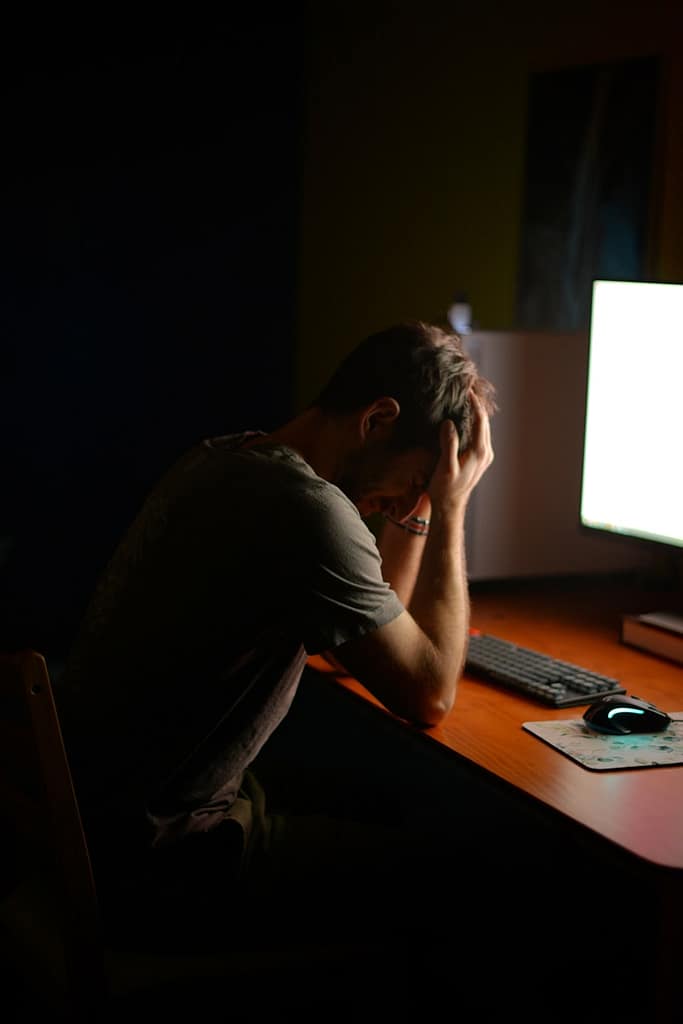 A person sitting at a desk with their head in their hands, overwhelmed and stressed, illustrating how tarot helps during moments of emotional burnout.