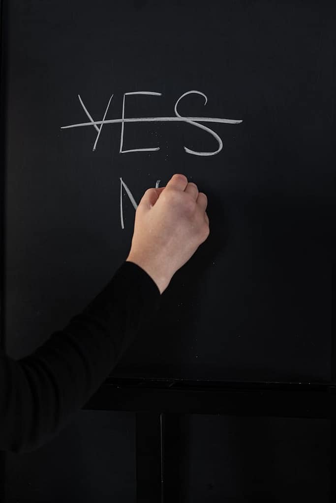 Hand writing on chalkboard with 'Yes' crossed out and 'No' written underneath, illustrating decision-making.