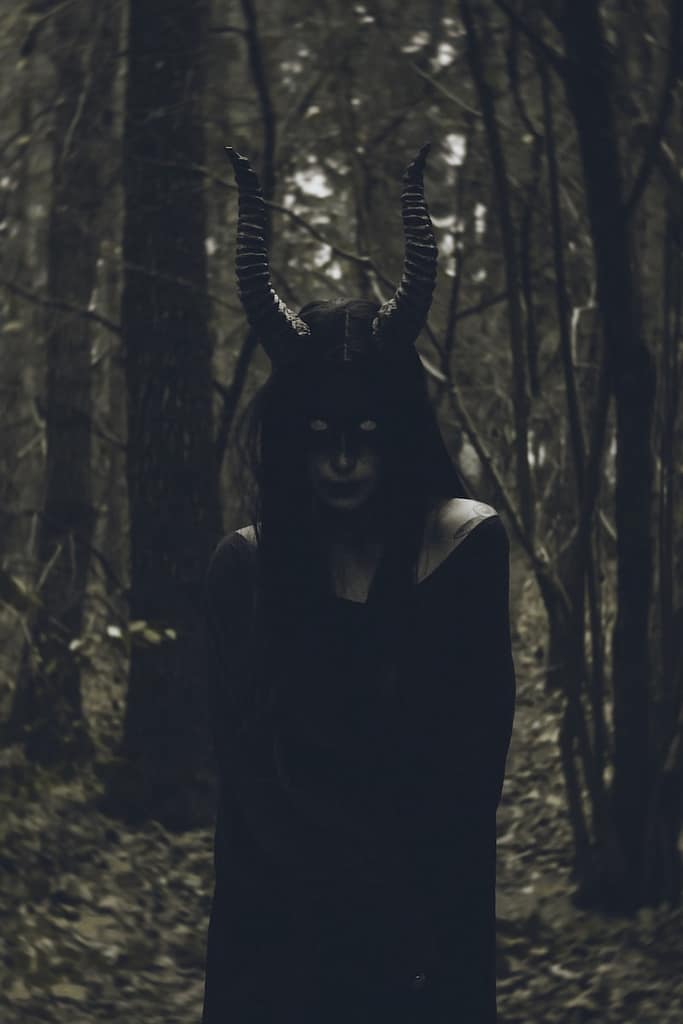A woman wearing a horned mask in the woods