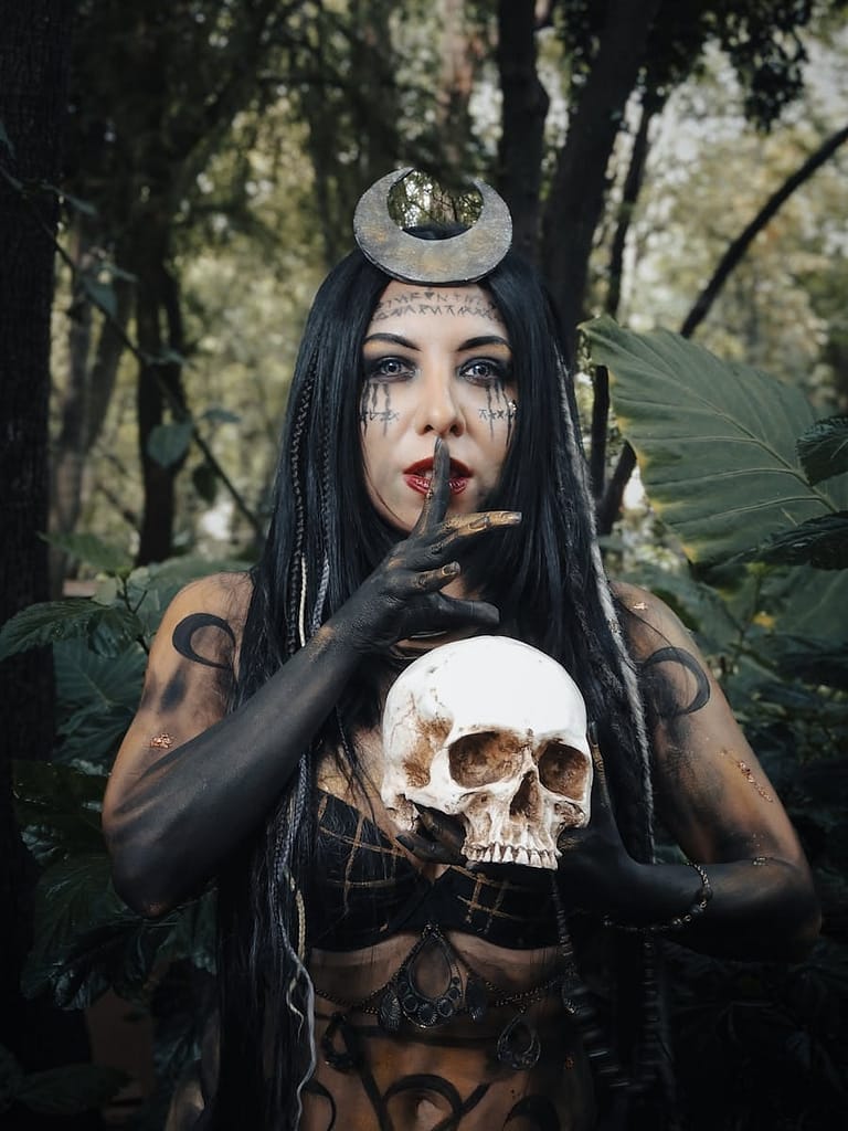 Mystic in dark witch attire posing outdoors with a skull.