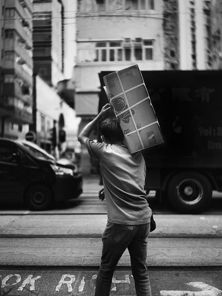 Black and white photo of a person carrying a heavy box in the city, symbolising the burden of carrying lies as truth.