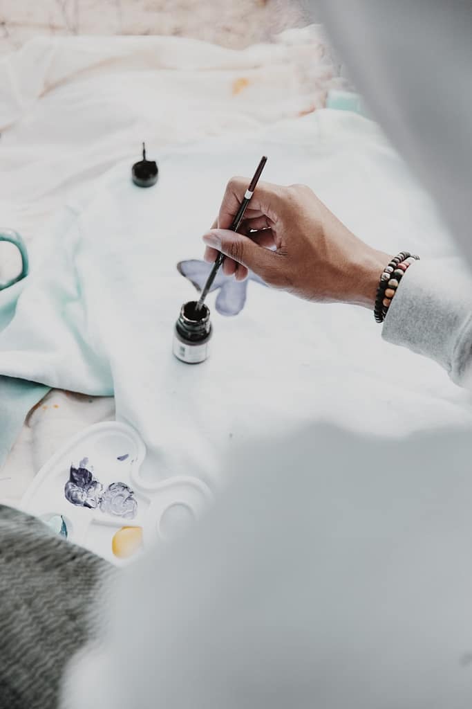 A close-up of a hand dipping a paintbrush into black ink, representing creative expression as a powerful way to release emotional pain and process feelings.