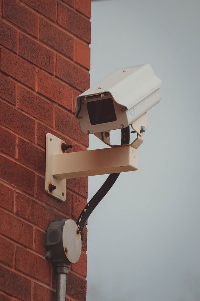 Surveillance camera on a brick wall symbolising tarot reader red flags, especially spying on third parties without consent.