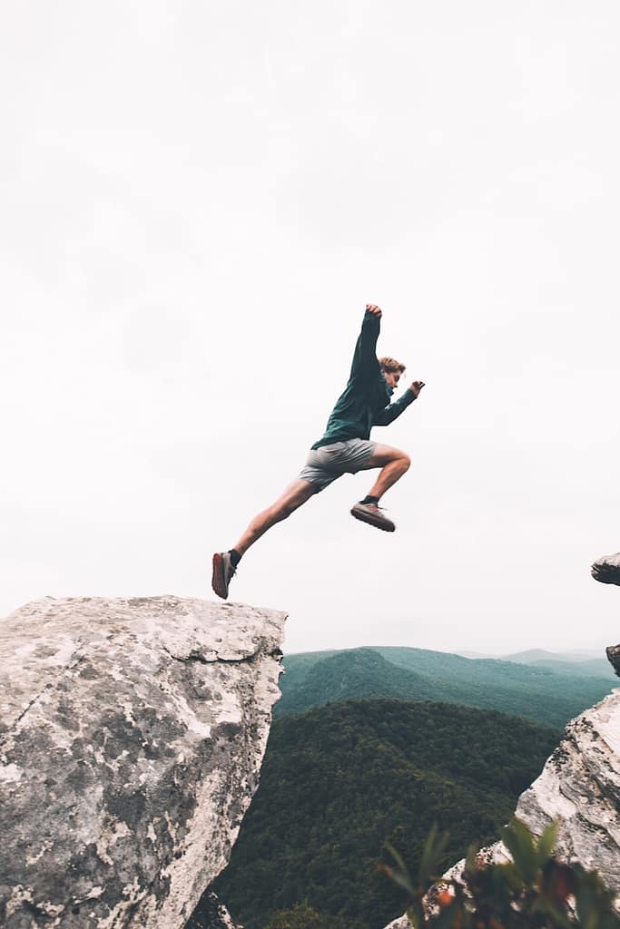 A person mid-air leaping between two cliffs over a vast landscape, symbolising the drama and risk of taking a big leap or making a drastic life change.
