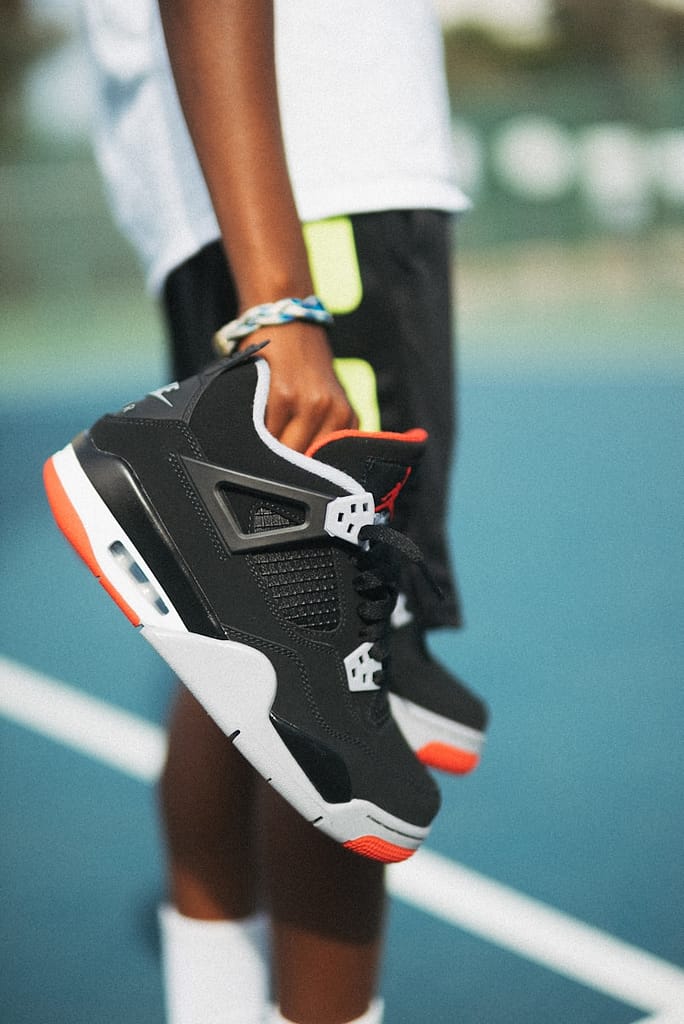 Close-up of a person holding a pair of trainers by the laces, standing on a sports court, symbolising the simplicity and power of small steps toward personal change.