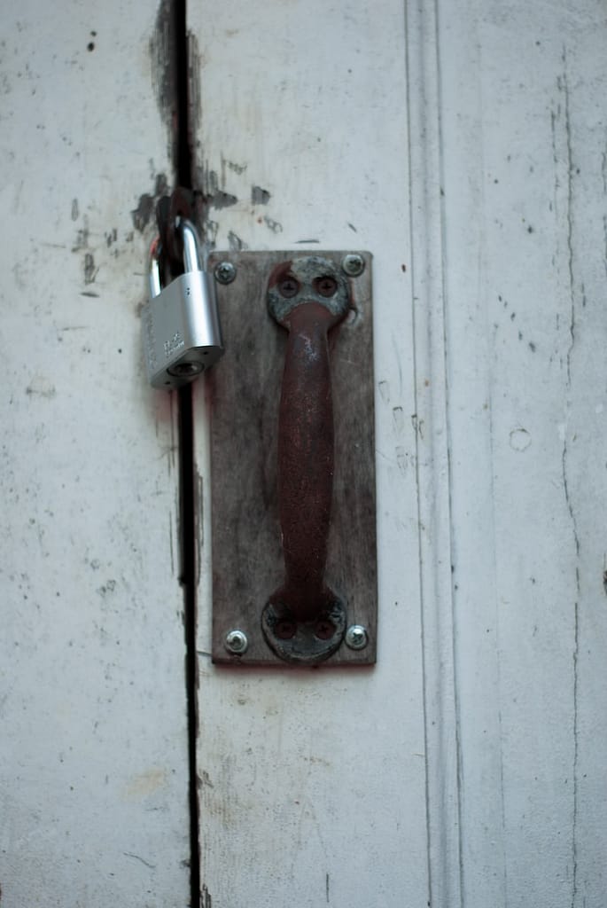 Padlocked wooden door with rusty handle, representing closed practices and restricted access to sacred traditions.