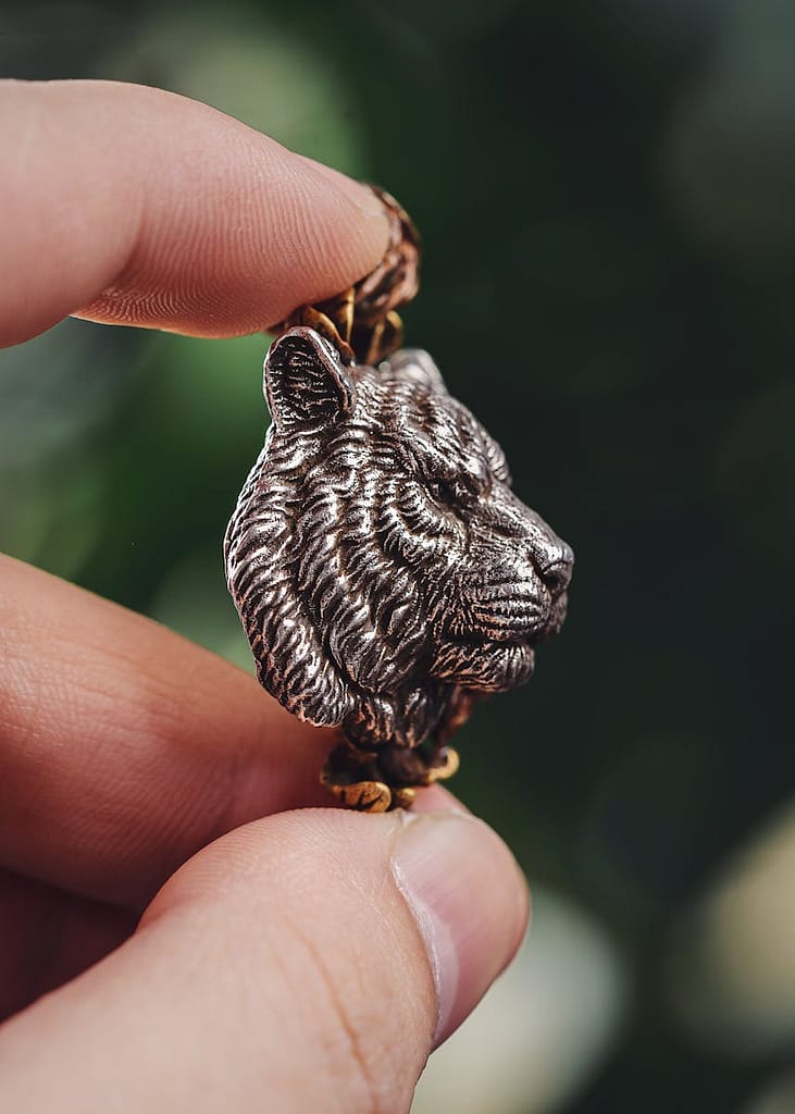 Close-up of a tiger pendant held between two fingers, representing the misuse of the term “spirit animal” in wellness and spiritual practices.
