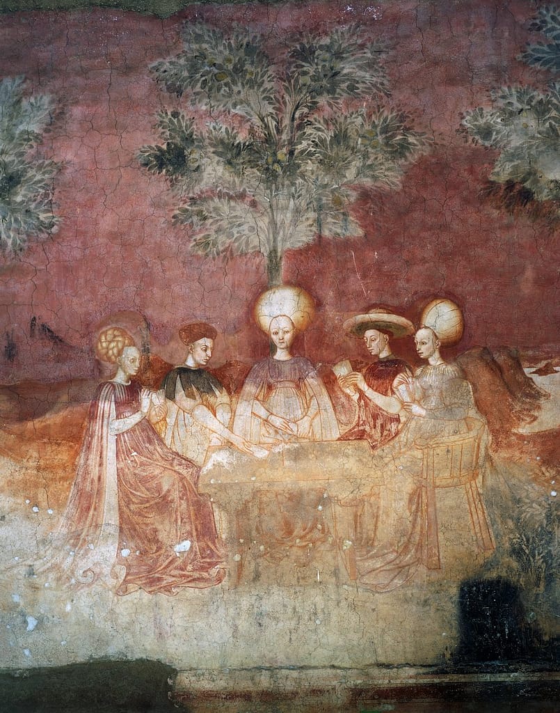 Fresco painting depicting five elegantly dressed Renaissance figures seated around a table beneath a tree, playing a card game. The scene features flowing garments, calm expressions, and warm earthy tones typical of 15th-century Italian art.