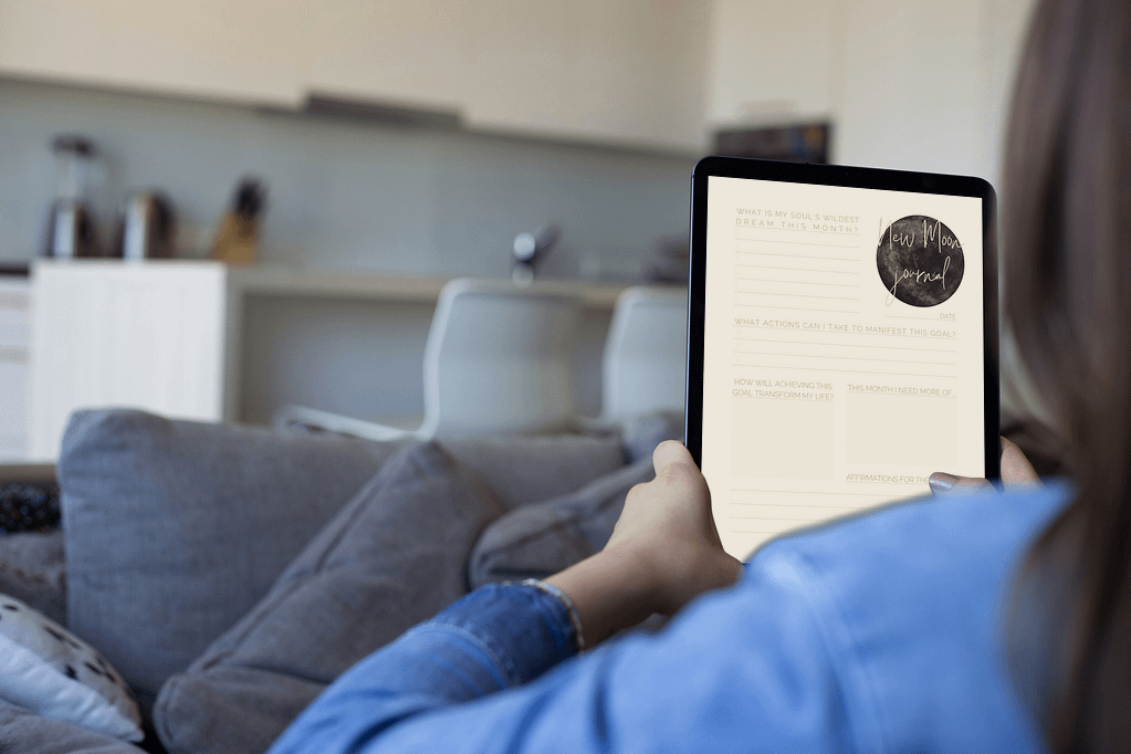 A person relaxing at home, using a tablet to complete the ‘new moon journal,’ focused on setting intentions for the upcoming lunar cycle.