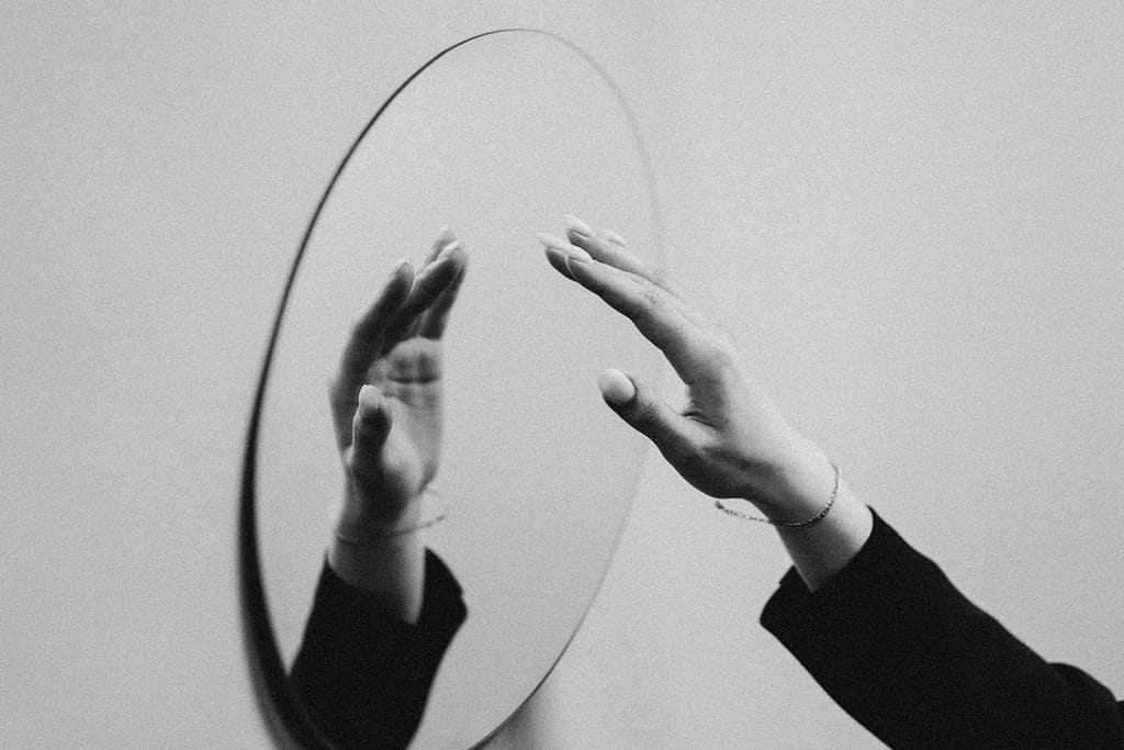 How The Enneagram And Tarot Work Together 2 A hand reaching toward its reflection in a mirror, symbolising self-discovery through the enneagram and tarot.