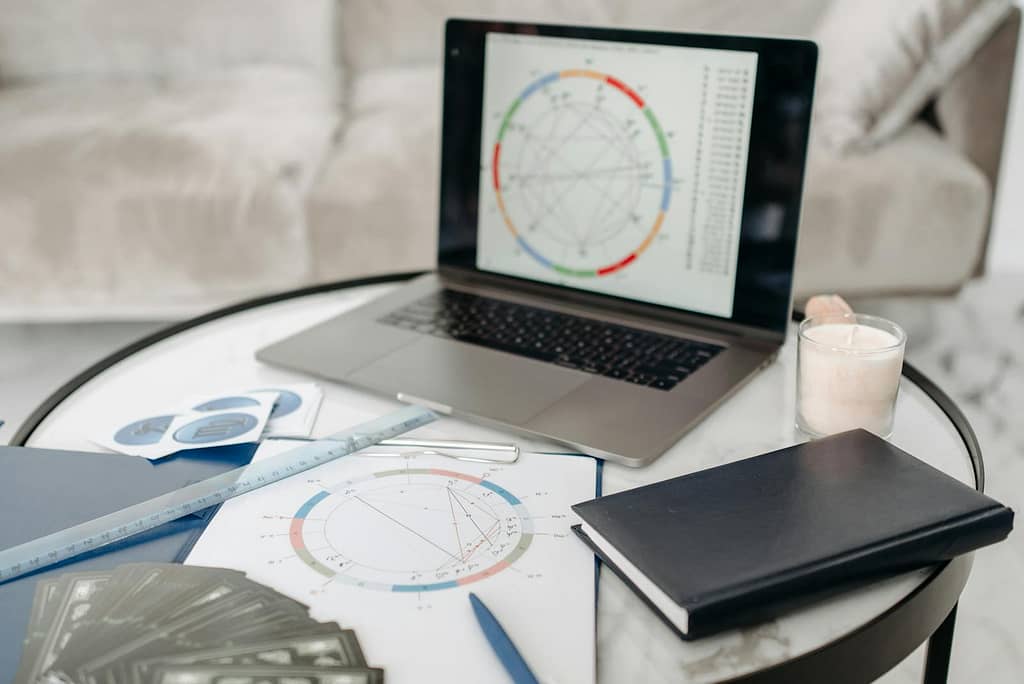 Four Ways to Explore Your Inner World: Find the Tool For You 3 Astrology charts displayed on a laptop next to tarot cards and notebooks on a table.