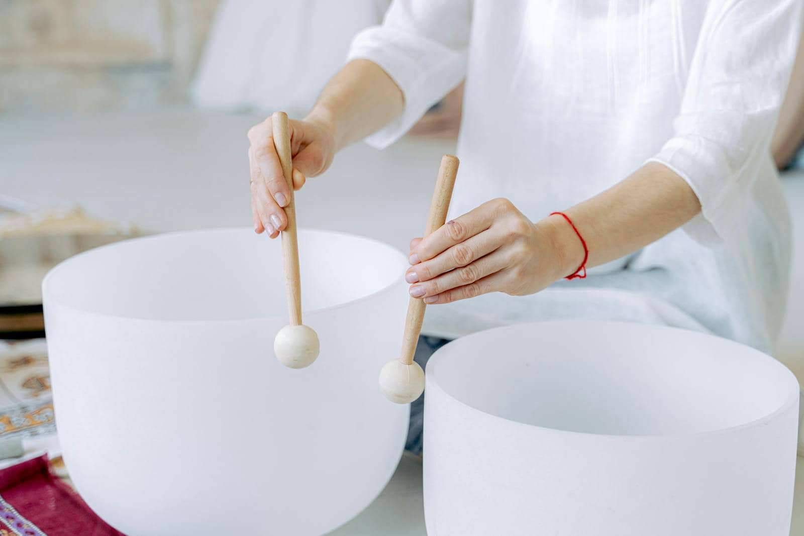 Hands playing crystal singing bowls with mallets, highlighting sound healing practice indoors. Person performing sound healing in Manchester using white crystal singing bowls and mallets.
