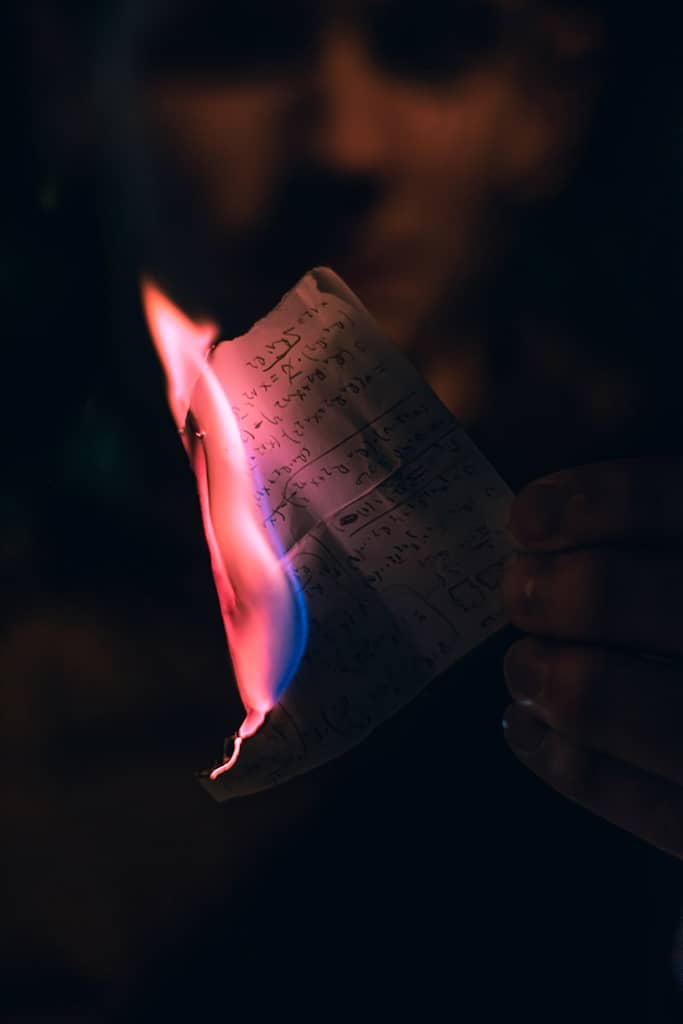 Person burning paper with writing.