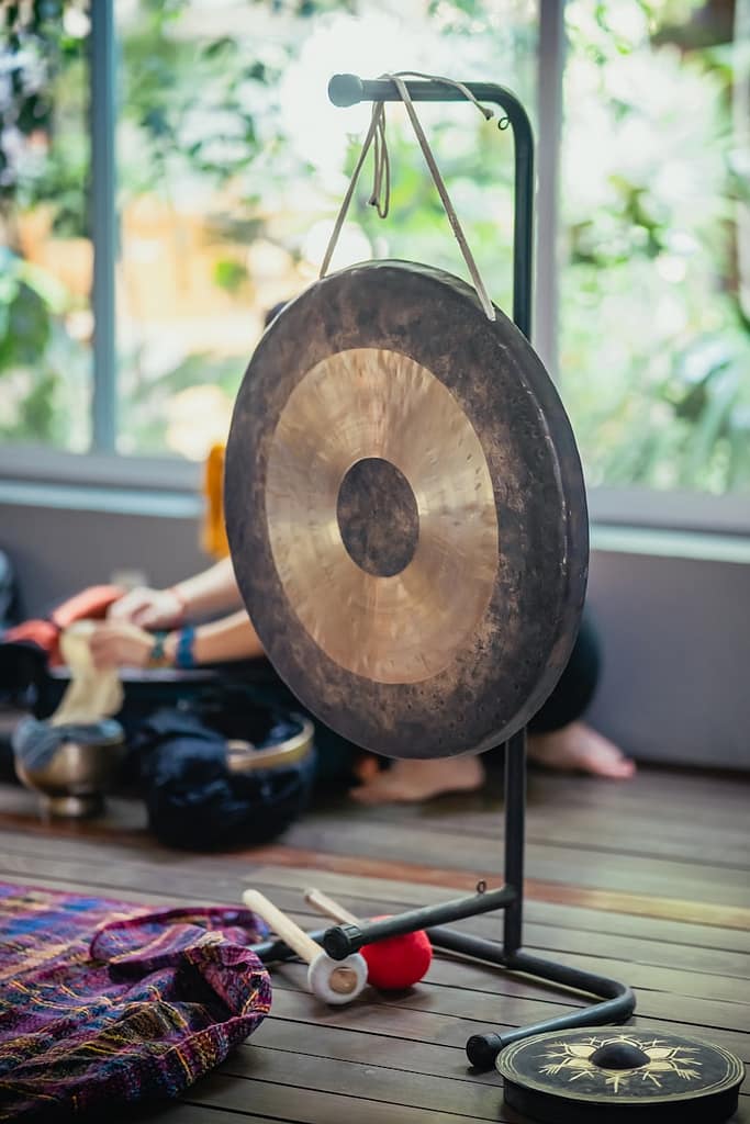 Gong and mallets set up for a sound healing session in Manchester, with instruments and participants in the background.
