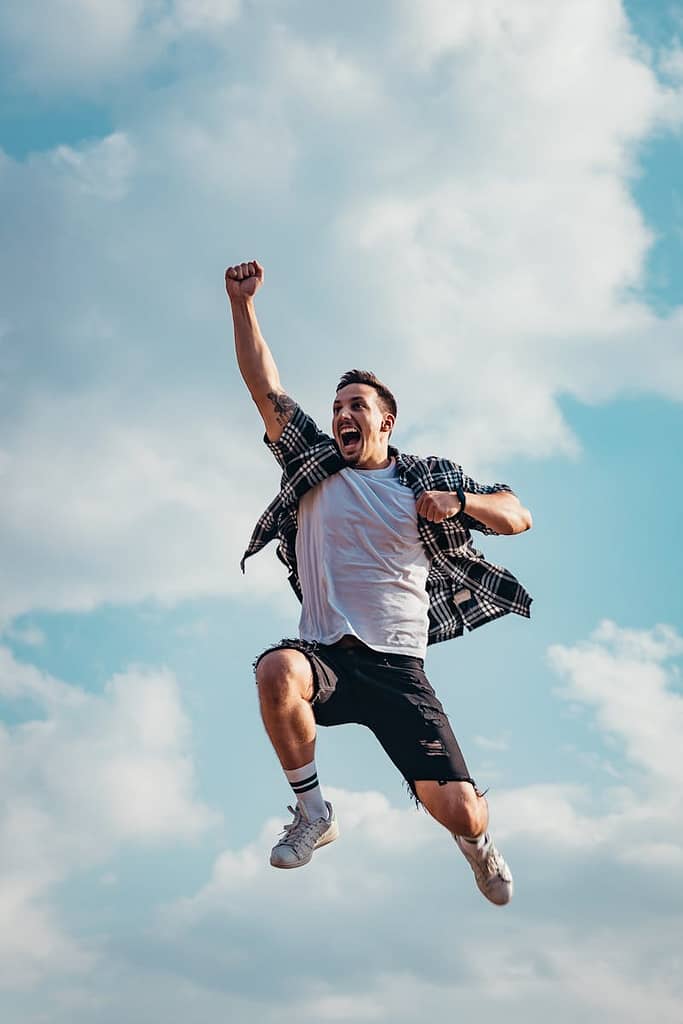 The Fool’s Journey: Life’s Growth And Transformation 2 A joyful young man jumps midair with clouds and blue sky in the background, exuding energy and freedom.