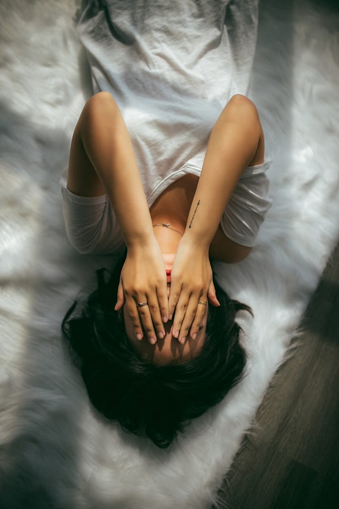 Person lying on the floor with hands covering their face, representing burnout from emotional labour and the cost of underpaid spiritual work