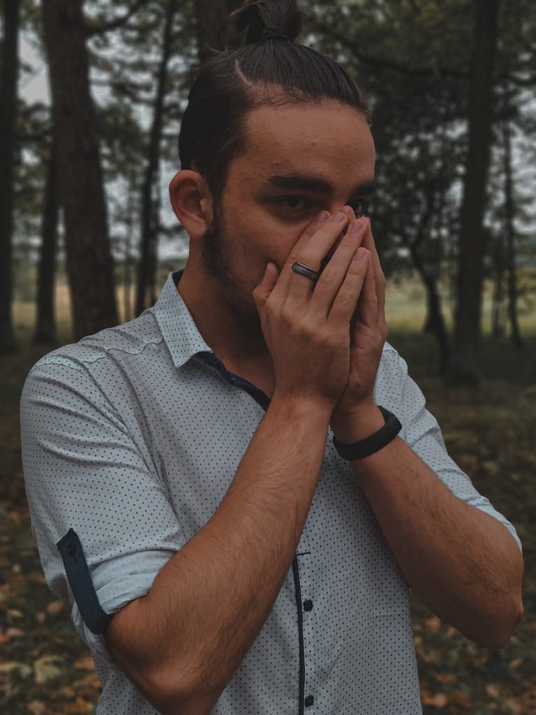 Person standing in a forest with hands covering their mouth, appearing deep in emotional reflection — a visual expression of how tarot can help you check in with yourself.
