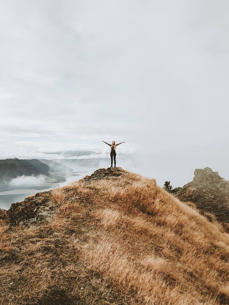 Person standing triumphantly on a mountaintop with arms raised, capturing the energy and creative spark of the suit of Wands and the power of reconnecting with your soul.