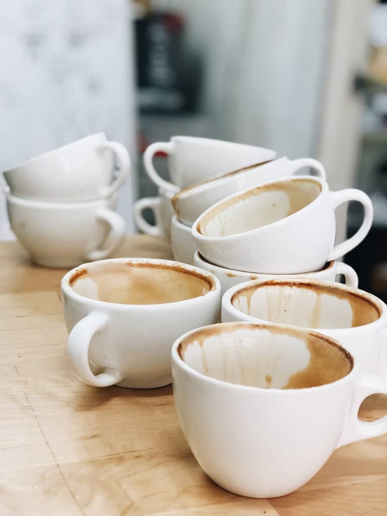 A pile of empty, stained coffee cups stacked on a wooden table, symbolising feeling emotionally drained and in need of a reset.