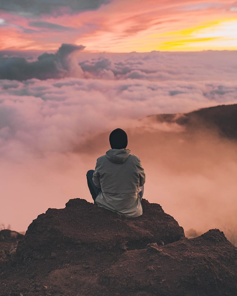 man meditating sitting on cliff