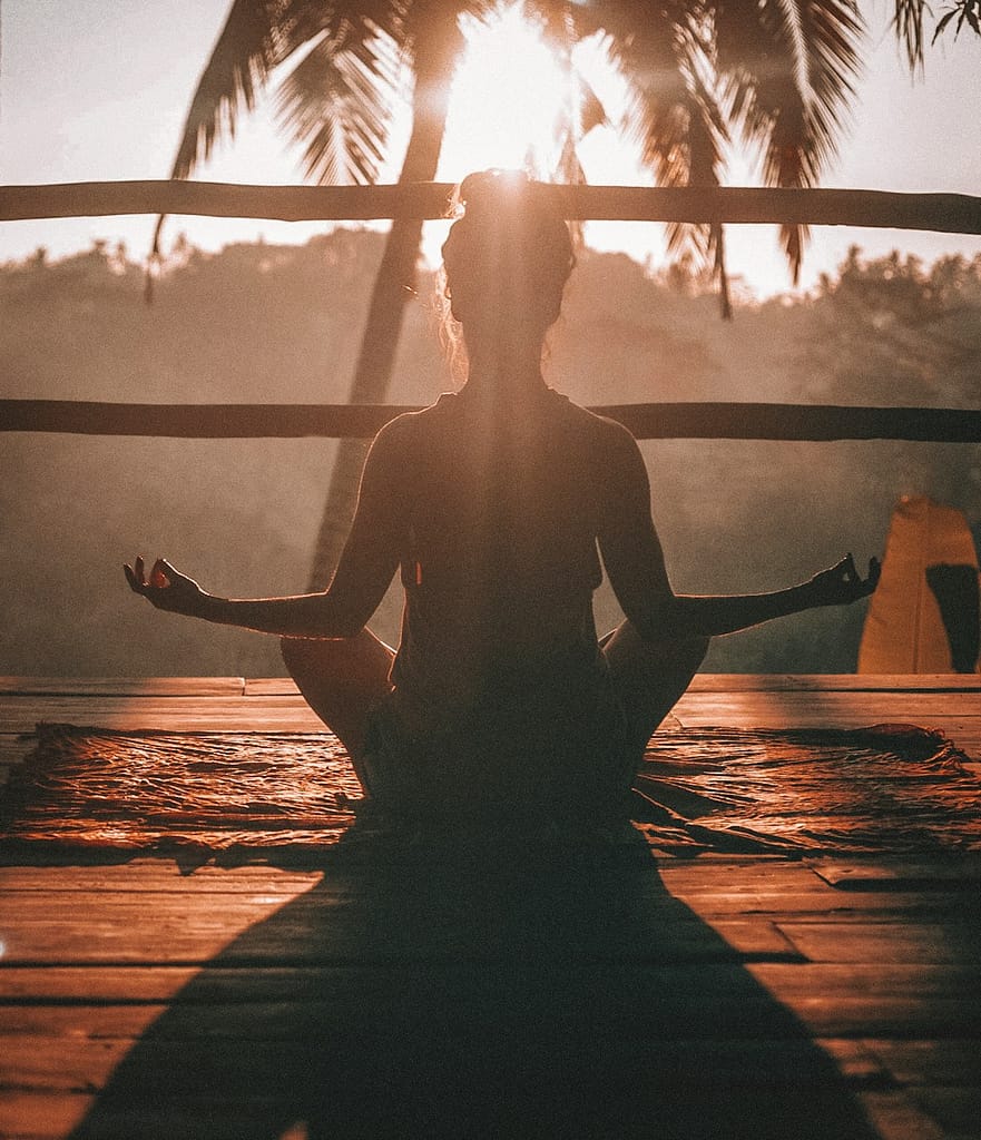 Silhouetted person meditating at sunrise, reflecting the spiritual focus of kundalini yoga and other types of yoga practices.